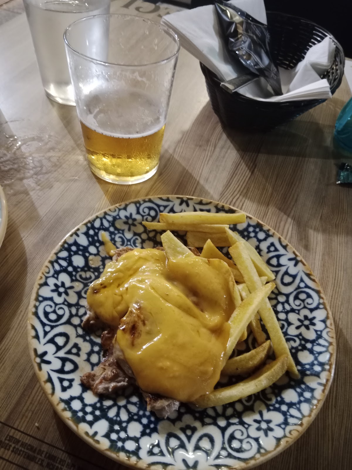 Carne con queso fundido y patatas paja, junto a una caña de cerveza