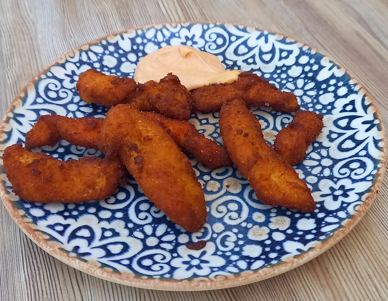 Tiras de pollo rebozado con salsa rosada en un plato de cerámica azul y blanca