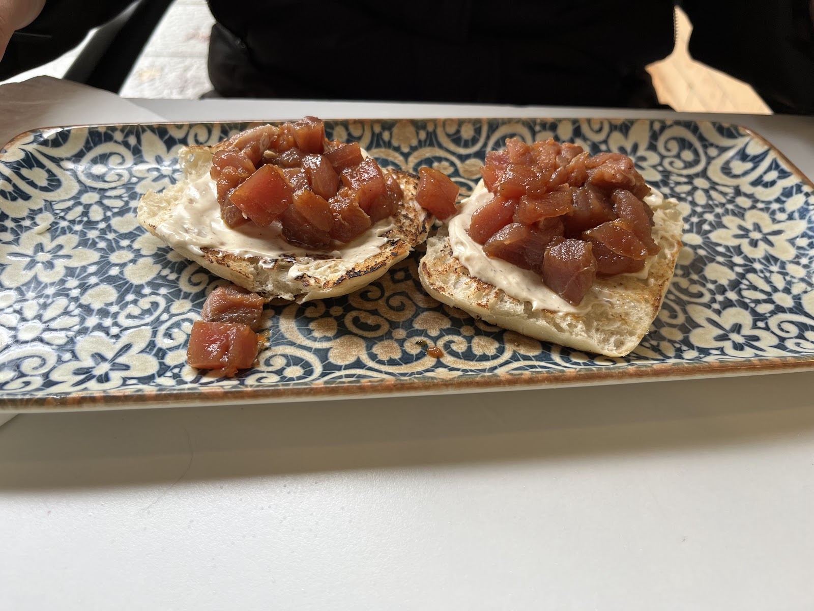 Dos tostas con crema de queso y dados de atún en una bandeja de cerámica
