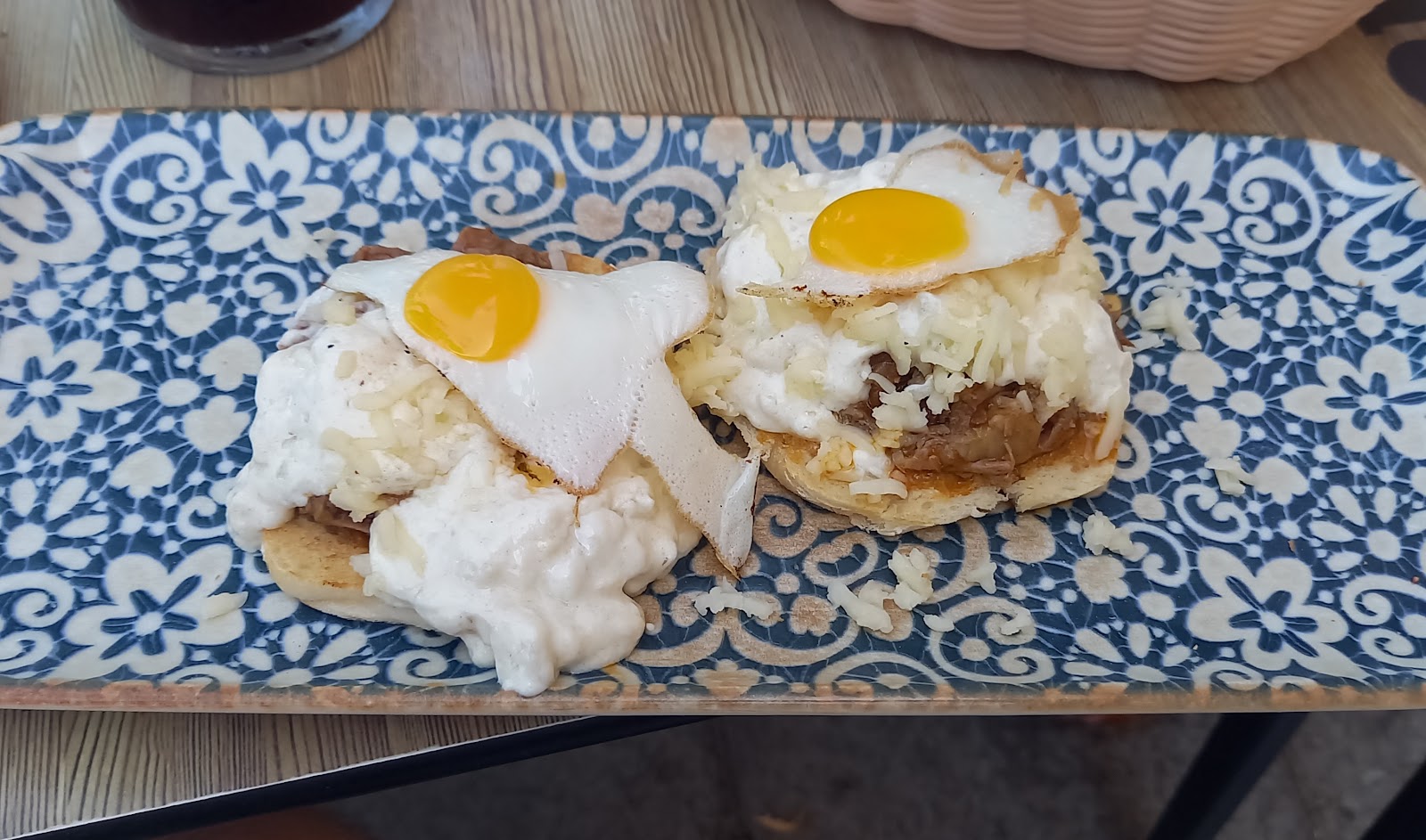 Dos tostas de carrillada con huevo de codorniz frito y queso rallado, sobre una bandeja de cerámica azul y blanca